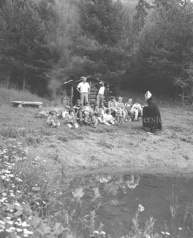 «Märchenprinz», Mann im Zaubererkostüm mit Kindergruppe bei Lagerfeuer bei Waldhütte am Seeufer