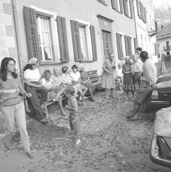Personen auf Bank und nebem Autos auf Dorfplatz
