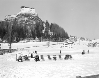 Personen auf dem Eis und auf Liegestühlen unterhalb Schloss Tarasp