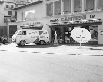 Lieferwagen und Frau vor Elektrogeschäft «radio CANTIENI tv», «Boutique Hüslihof» links und Parabolantenne rechts