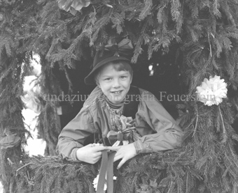 Chalandamarz, Knabe mit Schelle in mit Tannenzweigen dekoriertem Wagen