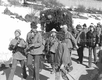 Chalandamarz, Knaben mit Schellen ziehen mit Tannenzweigen dekorierten Wagen