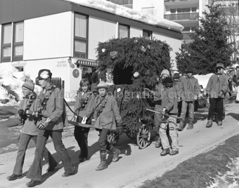 Chalandamarz, Knaben mit Schellen ziehen mit Tannenzweigen dekorierten Wagen