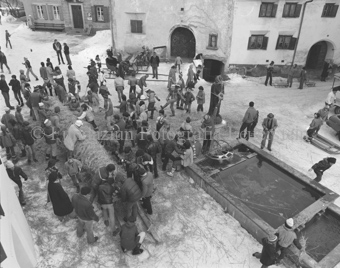 L'Hom Strom, Personen bauen Strohmann auf Dorfplatz neben Brunnen