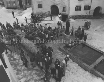 L'Hom Strom, Personen bauen Strohmann auf Dorfplatz neben Brunnen