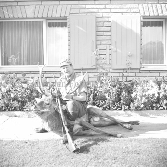 Mann hält geschossenen Hirsch am Geweih im Garten vor dem Haus
