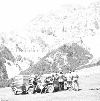 Personengruppe neben Landrover und Jeep auf Bergwiese, mit Anhängern mit Holzkäfigen