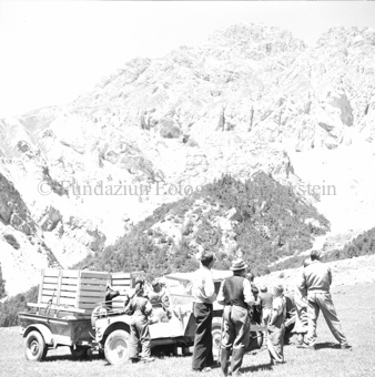 Personengruppe neben Landrover und Jeep auf Bergwiese, mit Anhängern mit Holzkäfigen