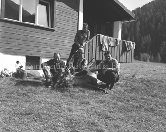 Vier Jäger mit Hirsch auf Wiese vor Haus