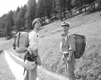 Zwei Gleitschirmflieger mit Schirmen in Rucksäcken zu Fuss auf Bergstrasse