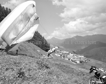 Gleitschirmflieger beim Start, Dorf im Hintergrund