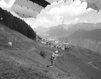 Gleitschirmflieger beim Start, Frau und Dorf im Hintergrund