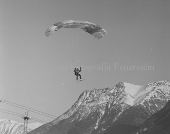Gleitschirmflieger mit Ski in der Luft, Berge und Seilbahn im Hintergrund