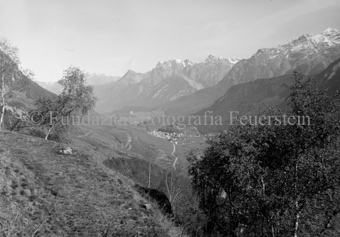 Blick ins Tal zwischen zwei Bäumen durch, Ardez mit Ruine Steinsberg, Schloss Tarasp im Hintergrund