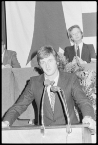 Politiker am Rednerpult, rechts von ihm Parlamentspräsident Roland Béguelin, im Hintergrund grosse Jura-Fahne