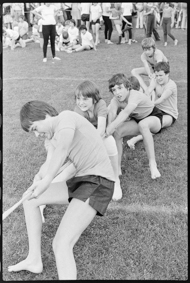Kinder in Turnkleidung am Seilziehen auf Rasen, im Hintergrund Zuschauende