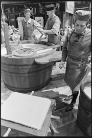 Drei Männer in Kleidung von früher beim Papier schöpfen aus grossem Holz-Bottich, im Hintergrund Bühne mit Musikern und Firmenschild der «Papierfabrik Cham AG»