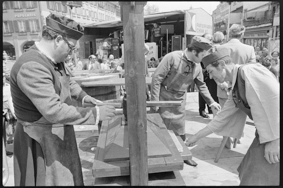 Drei Männer in Kleidung von früher bei der Arbeit mit einer Papierpresse, im Hintergrund Schaulustige, Bühne mit Musikern und Firmenschild der «Papierfabrik Cham AG»
