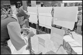 Mann in Kleidung von früher beim Aufhängen von geschöpftem Papier zum Trocknen, im Hintergrund Schaulustige
