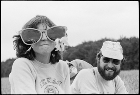 Velofahrerin mit grosser Sonnenbrille und Blume, Velofahrer mit Hut und Aufschrift «Housi»