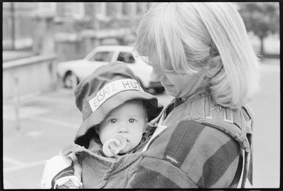 Frau mit Kleinkind, welches einen Hut trägt (Aufschrift «ERSATZ HUT», vielleicht Hut von Hansueli Trachsel)