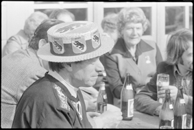 Besucher des Anlasses beim Biertrinken, ein Mann in Tracht und mit Berner Wappen dekirierter Hut