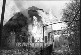 In Flammen stehendes Haus, ringsum heruntergefallene Ziegel