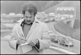 Mann mit Notizbuch, im Hintergrund Autokolonne auf der Zufahrtsstrasse zur Verladestation nach Goppenstein und Brig-Iselle