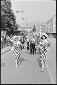 Umzug mit Ehrendamen, Fahnenträger und Musikgesellschaft, im Hintergrund Bahnhofplatz Biel