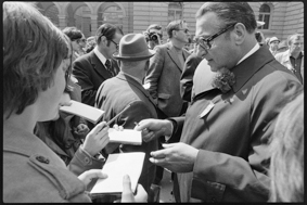 Stadtpräsident Reynold Tschäppät im Gespräch mit Schülern auf dem Bundesplatz, am Mantel steckt das 1. Mai-Abzeichen 1976 und eine Nelke