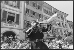 Umzug in der Hauptgasse: Mann in Verkleidung als Uristier mit Horn-Instrument, am Strassenrand viele Zuschauende