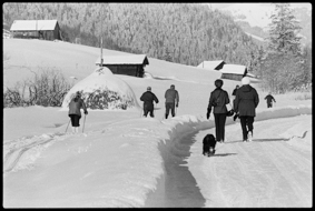 Menschen auf Langlaufloipe und auf Spazierweg in tief veschneiter Landschaft, Ställe und Heustock