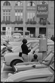 Parkierte Autos neben Ticket-Automat und Hinweistafel, im Hintergrund die Kantonalbank