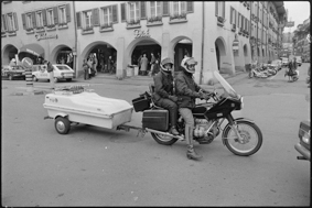 Motorrad über den Waisenhausplatz fahrend, im Hintergrund Kleidergeschäfte Weilenmann und Dick, davor Taxistand mit 2 Taxis (3 x 24 und 3 x 45), rechts im Bild die Neuengasse