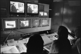 Fernseh-Mitarbeitende am Sendepult, vor ihnen mehrere Monitore