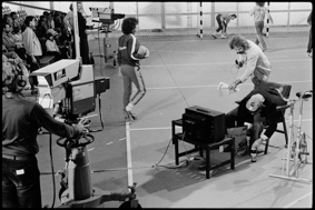 Moderator Walter Däpp mit Mikrophon, zwei Kameras der ETS (Eidg. Turn- und Sportschule), im Hintergrund Handballspieler und Zuschauer
