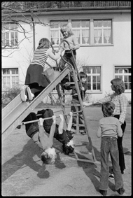 Kinder beim Spiel auf der Rutschbahn unter Aufsicht einer Lehrerin
