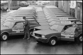 Zahlreiche parkierte Neuwagen, Werbung auf Autotüren, Firmenschilder der Th. Willy AG