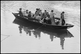 Fährschiff mit Bootsführer und Passagieren, im Hintergrund Kiesstrand