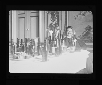 Mann, sitzend am Tisch mit mehr als zwei Dutzend leeren Weinflaschen