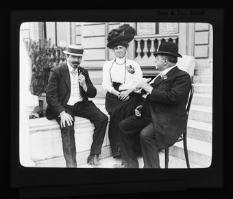 Eine Frau mit zwei Männern, sitzend vor einem Haus