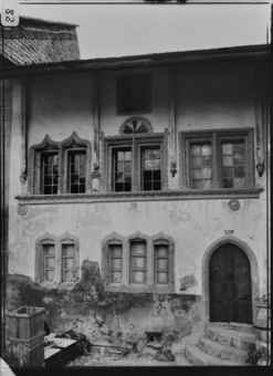Fassade von zweistöckigem, weiss verputztem Steinbau erhöhter Eingang mit Rundbogen, Fenster mit Kielbogen und Steinbildhauerei
