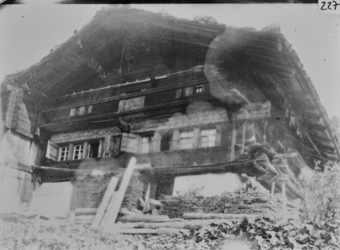 Giebelseite zweistöckiger Holzbau mit gemauertem Fundament, geschindeltem Satteldach vor dem Gebäude aufgeschichtete Schindeln