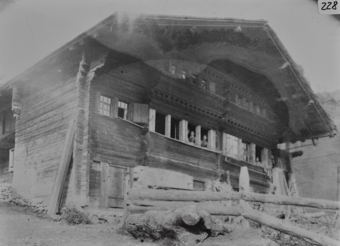 Dreistöckiges Holzgebäude mit Satteldach drei aus den Fenstern im 1 OG. schauende Frauen, Giebelseite mit Friesen verziehrt