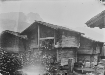 Mehrere Speicher in Blockbauweise mit Satteldach vier Kinder auf Obergeschosslaube sitzend, darunter Frauen und Kinder neben steiler Treppe sitzend