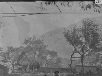 Ortsaufnahme mit mehreren schiefergedeckten Gebäuden, mittig in die Kamera schauender Knabe mit Hut