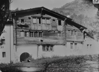Giebelseite dreistöckges Wohnhaus mit gemauertem Erdgeschoss, Obergeschoss gezimmert, geschindeltes Satteldach mehrere seitliche Anbauten, links Eingangsbogen, im Hintergrund Bergzug