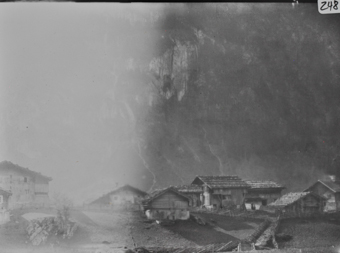 Mehrere Holzgebäude mit Pultdächern, zwischen Gebäuden Schrankzaun, im Hintergrund Felswand