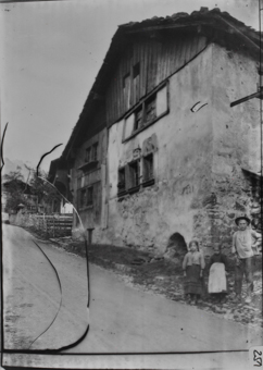 Dreistöckiges, gemauertes Gebäude an steiler Strasse, gezimmerter, zweistöckiger Anbau, Giebelseite mit Holzschalung, rechts an Hausecke stehend zwei Mädchen und ein Junge
