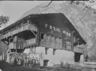 Dreistöckiges Wohngebäude mit gemauertem Erdgeschoss und gezimmertem Oberbau, geschindeltes Schleppdach, Eingang traufseitig im 1. OG mit Treppe und Windfang, darüber Obergeschosslaube, eine Gruppe von 17 Kindern vor dem Gebäude stehend, rechts daneben zwei Frauen vor Bretterzaun
